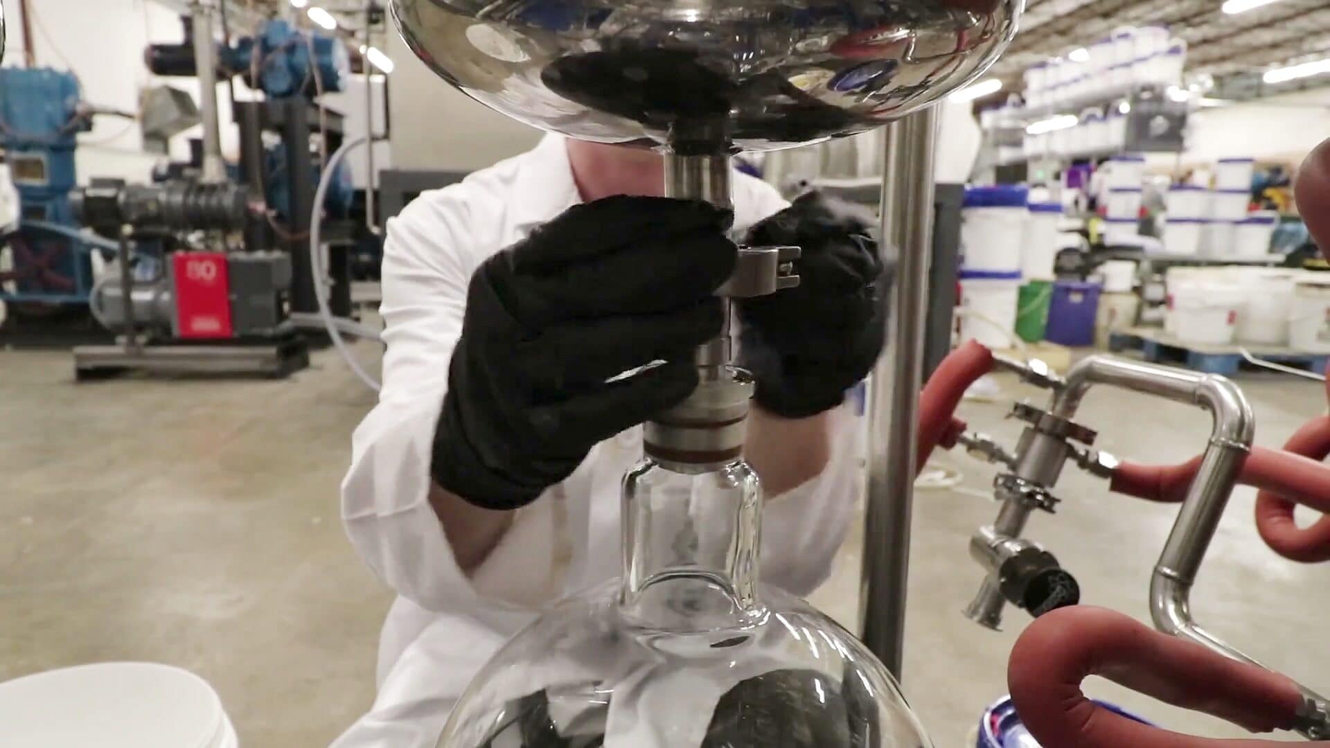 An operator in gloves and a lab coat fitting a glass flask to a stainless line