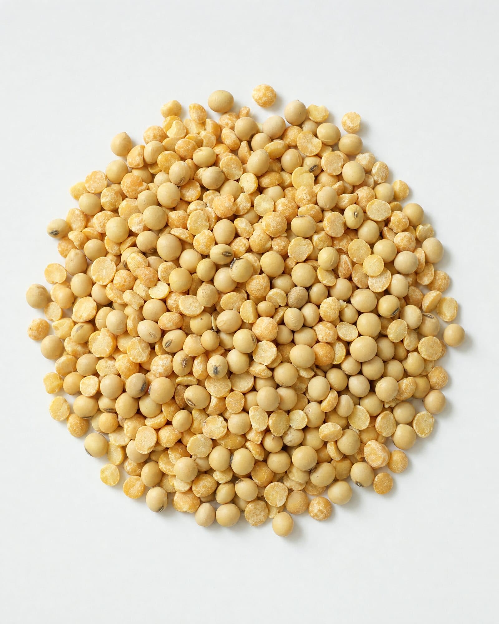 Yellow split peas and soybeans in a mound on a white surface