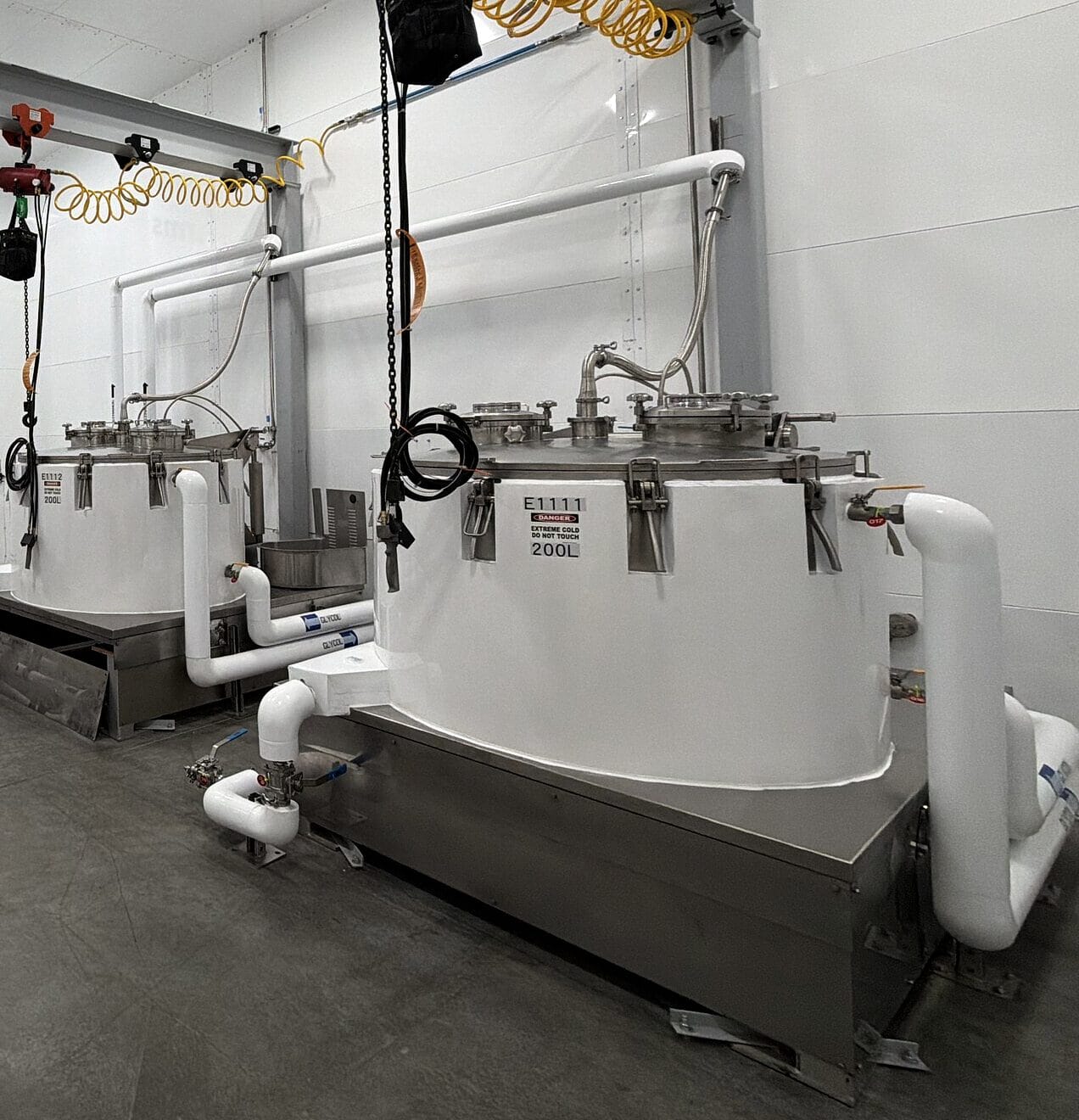 The extraction room in Loveland: white jacketed vessels on stainless drip pans under an overhead hoist